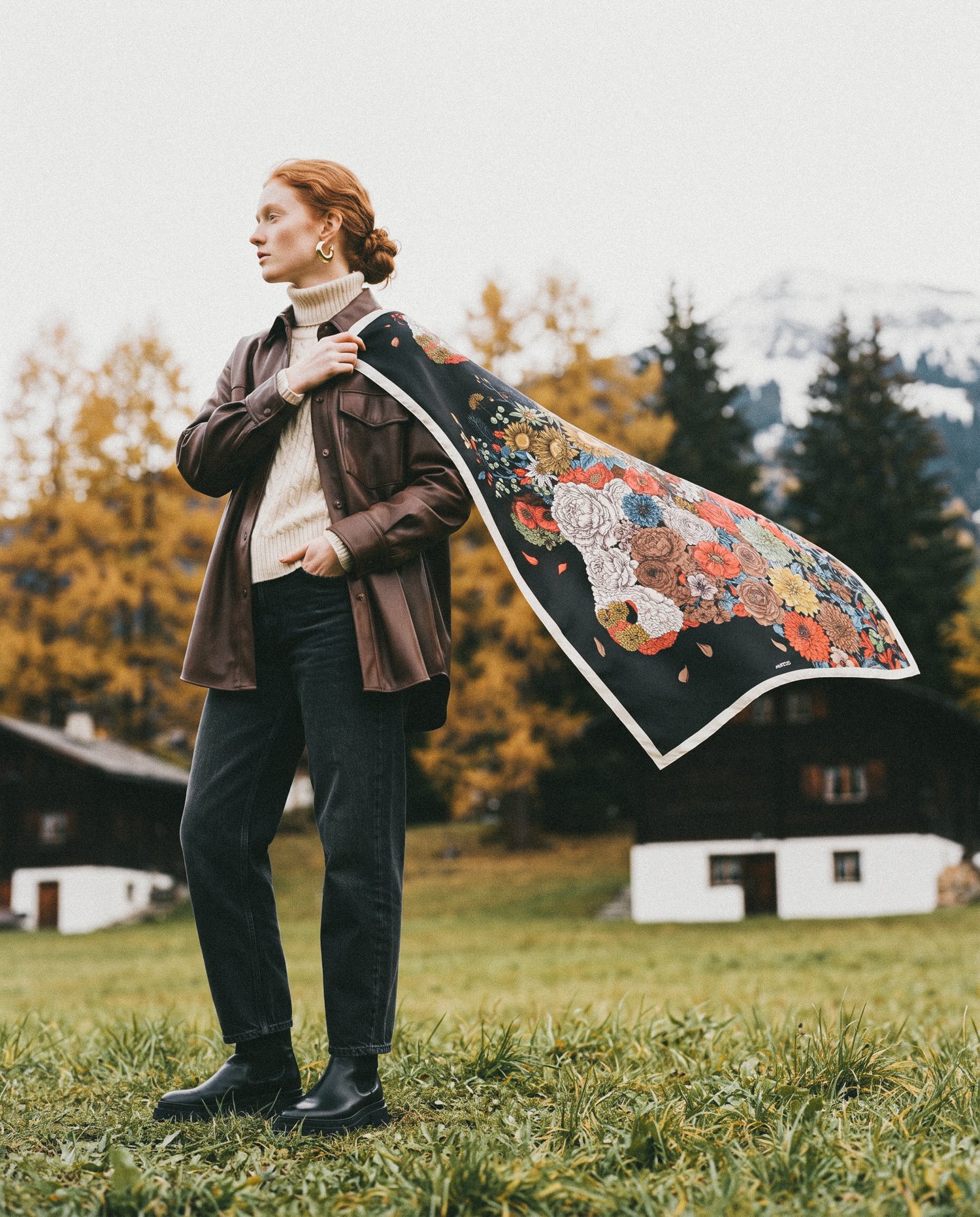 A woman in an alpine meadow near Gstaad holding the La Désalpe silk scarf as it lifts in the wind